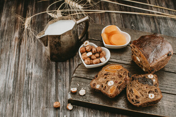 a mug of milk, bread with dried fruits, nuts and dried apricots on a dark background 
