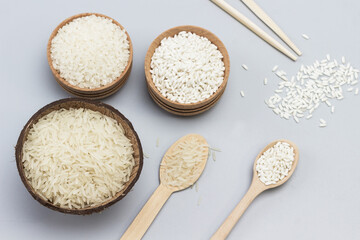 Three types of white rice in wooden bowls and coconut shells. Wooden spoon with rice and sticks