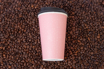 coffee cup which is pink with white  dots in the background of coffee beans