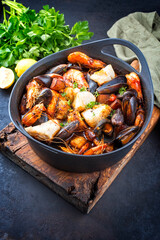 Traditional French seafood bouillabaisse with fish, king prawns and mussels in tomato sauce as close-up on a modern design pot