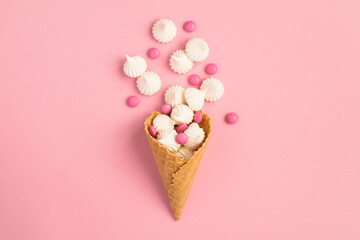 Top view of ice cream cone with white meringue and candy on the pink background