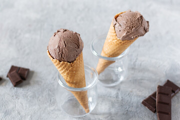 Balls of chocolate ice cream in a waffle cones in a glass jar on grey background.