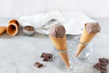Balls of chocolate ice cream in a waffle cones in a glass jar on grey background.