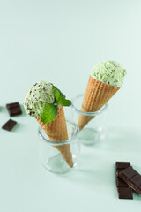 Scoops of mint ice cream with chocolate crumbs in a waffle cones on light green background.