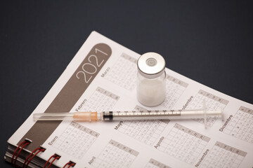 syringe and vaccine canister, with calendar 2021, blue background