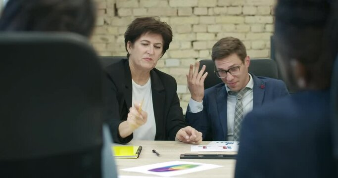Caucasian woman and African American man whispering at business meeting. Serious nervous CEO throwing pencil and scolding coworkers in office. Stress and overworking. Cinema 4k ProRes HQ.
