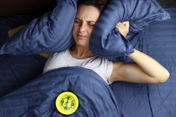 alarm clock wakes up a girl who covered her ears with pillows