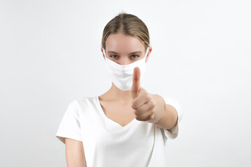 Young white woman wearing protection face mask showing in front of her thumb. Virus, covid-19, coronavirus.