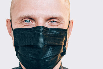 Portrait of man smiling through a black facial mask during a COVID-19 world pandemic looking at camera. Self-protection and stop virus spreading measures concept image