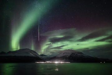 Northern lights and a shooting star above snow-covered mountains by the sea