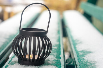 Snow covered street bench and candle in black candlestick in new year season
