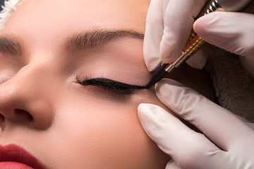 Permanent eye makeup close up shot. Cosmetologist applying tattooing of eyes. Makeup eyeliner procedure - obrazy, fototapety, plakaty
