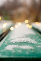 Snow covered street bench and bokeh of yellow garland in new year season