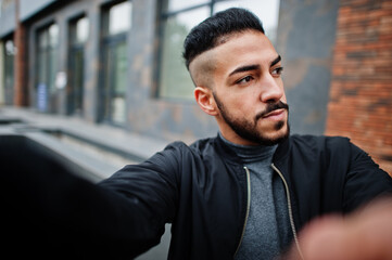 Obraz premium Portrait of stylish arab beard man wear grey turtleneck and black jaket. Arabian model guy make selfie by camera.