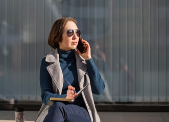Fototapeta premium business woman with notebook and phone sitting in the autumn city