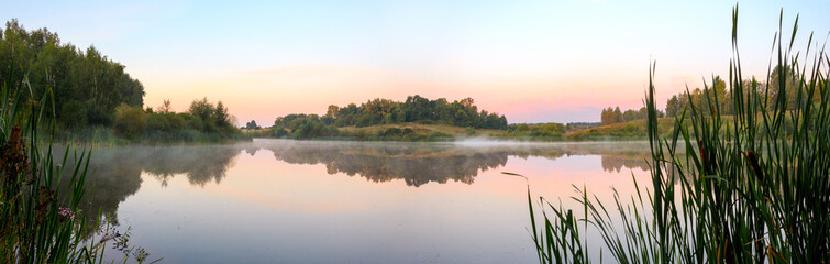 Obraz na płótnie Canvas Panoramic view of calm lake during foggy sunrise.