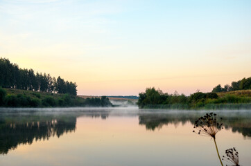 Tranquil landscape with calm lake during foggy sunrise.