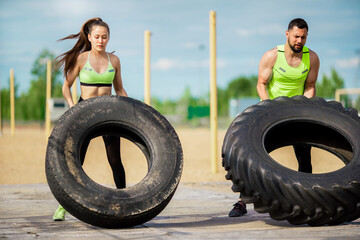 Powerful exercising of young athletic couple outside. Young girl and guy lifting tyres outside. © Georgii