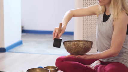 Woman playing on Tibetan singing bowl while sitting on yoga mat. Vintage tonned.