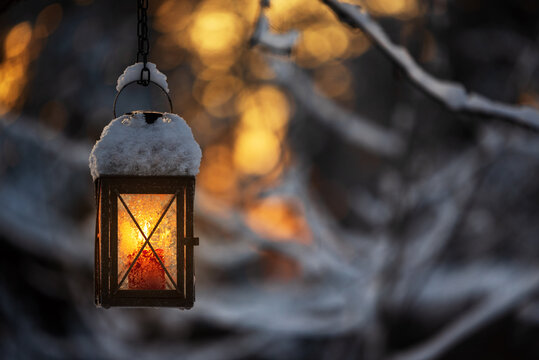 Candle lantern hanging from tree branch, bokeh winter background.