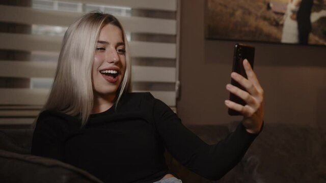 Sweet blonde woman sitting on the sofa while looking at her phone is suddenly surprised, lifestyle, technology, communication and social media concept