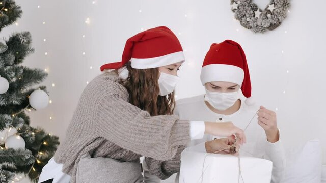 Christmas or New Year celebration. Covid-19 pandemic. The mother ans her son in party hats are unwrapping the gifts near Christas tree.