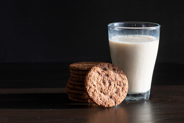 Serving healthy morning breakfast with a fresh milk in a glass and Pile of Delicious Chocolate homemade Chip Cookies on a vintage dark background. Food and Flowers Aesthetic composition
