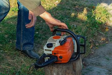 An elderly man's hands close the cover of the chainsaw refueling hole.