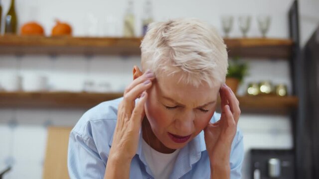 Sick senior woman touch head suffering from headache and coughing at home