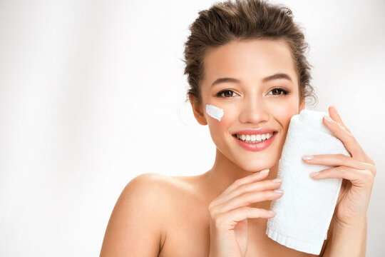 Woman wiping facial skin with towel, removing cream. Photo of woman with perfect skin on white background. Beauty and skin care concept