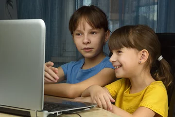 Poster Twee meisjes kijken naar de laptop en glimlachen. Concept van thuisonderwijs op afstand. © Albert Ziganshin
