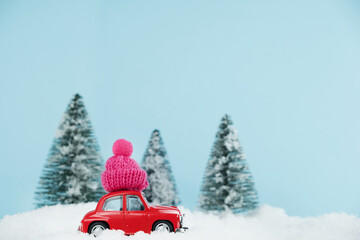 Christmas red car with knitted pink hat in a snowy pine forest. Space for text. Happy New Year card concept