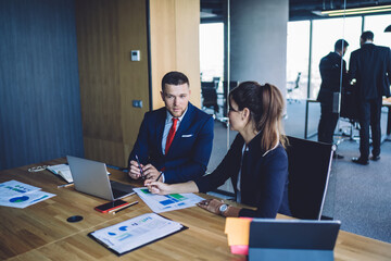 Caucasian male and female colleagues collaborating on paper documents with financial infographics of capital monetary gain, professional experts brainstorming on revenue graphics discussing briefing