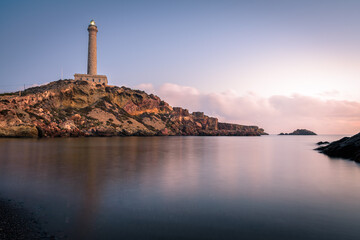 Lighthouse of Cabo de Palos reflected in the water of the beach at sunrise, Murcia, Spain