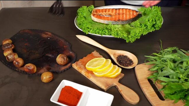 Woman's hand adds potatoes on the fried salmon on the plate with lettuce .