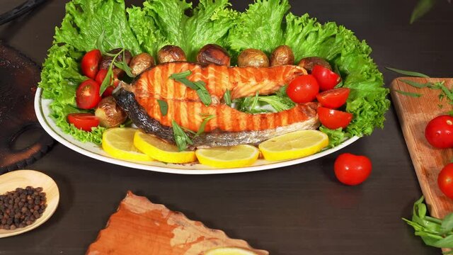 Woman's hand adds tarragon herbs on the fried salmon on the plate with lettuce , potatoes and tomatoes.