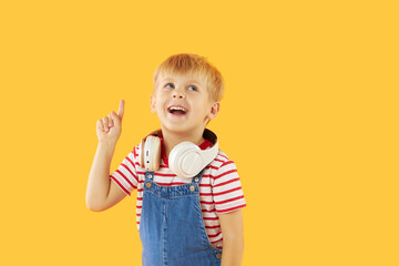 Smiling child boy enjoys listens to music in headphones over colorful yellow background. Vivid and fun emotions, happy child with pleasure listens to songs in wireless headphones..