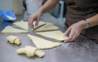 Young woman making croissants in bakery