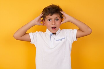 little cute Caucasian boy kid wearing white t-shirt against yellow wall covering eyes with both hands, doesn't want to see anything or feeling ashamed. Human feelings reactions.