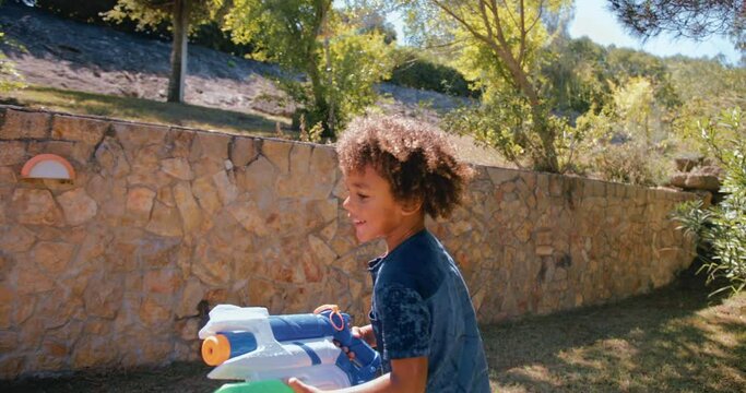 Boy running and playing with water gun in the garden