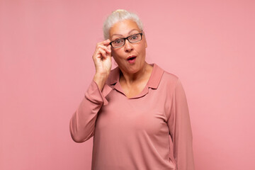 Surprised senior woman looking through glasses otices something unexpected,