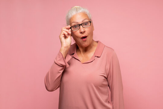 Surprised senior woman looking through glasses otices something unexpected,