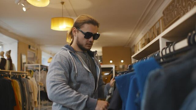 Young man in sunglasses hiding jeans in jacket at clothes store