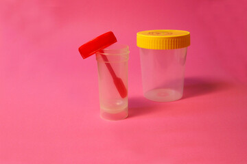 close open red fecal container and closed plastic with a yellow lid container for collecting urine and semen on a pink background side view