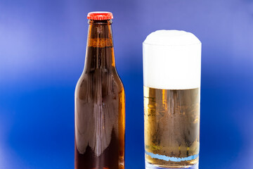 Vaso de cerveza y botella sobre fondo azul