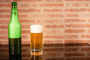 Vaso de cerveza y una botella verde sobre una mesa y fondo rústico