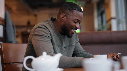 African American man online chatting using smart phone sitting in a cafe - Powered by Adobe