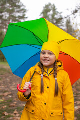cute beautiful teenage girl in an orange pants, raincoat and hat with rainbow-colored umbrella. Cosiness, autumn