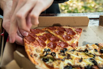Un hombre (solo muestra la mano) cogiendo una porción de pizza pepperoni en su caja de cartón
