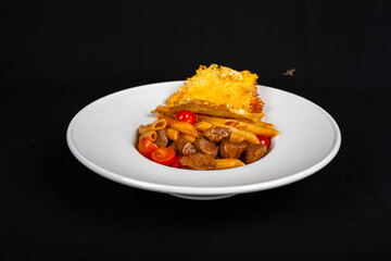 Pieces of meat with pasta on plate and black background